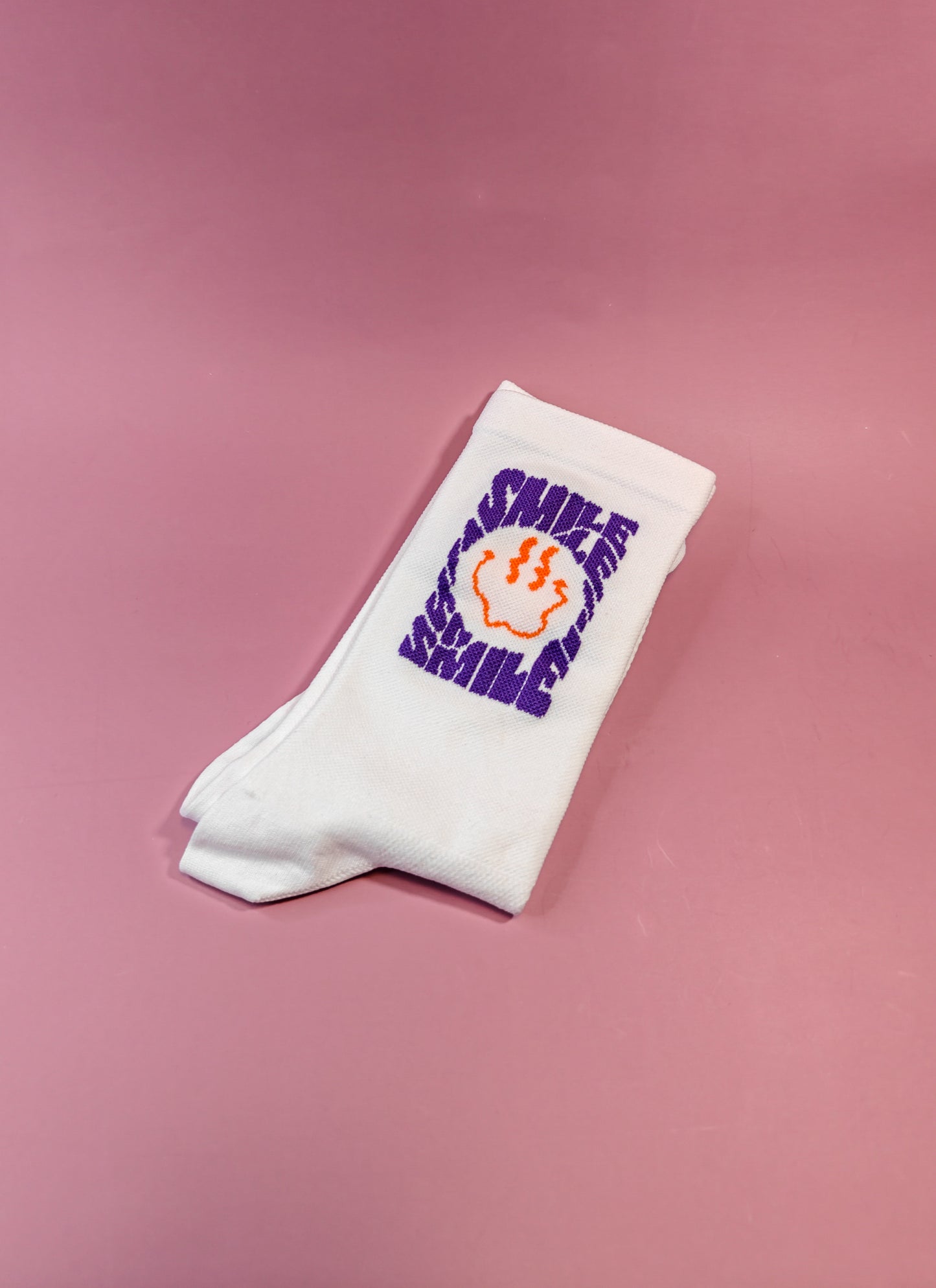 Witte sokken met paarse 'SMILE' tekst en oranje smiley op roze achtergrond, cadeau idee