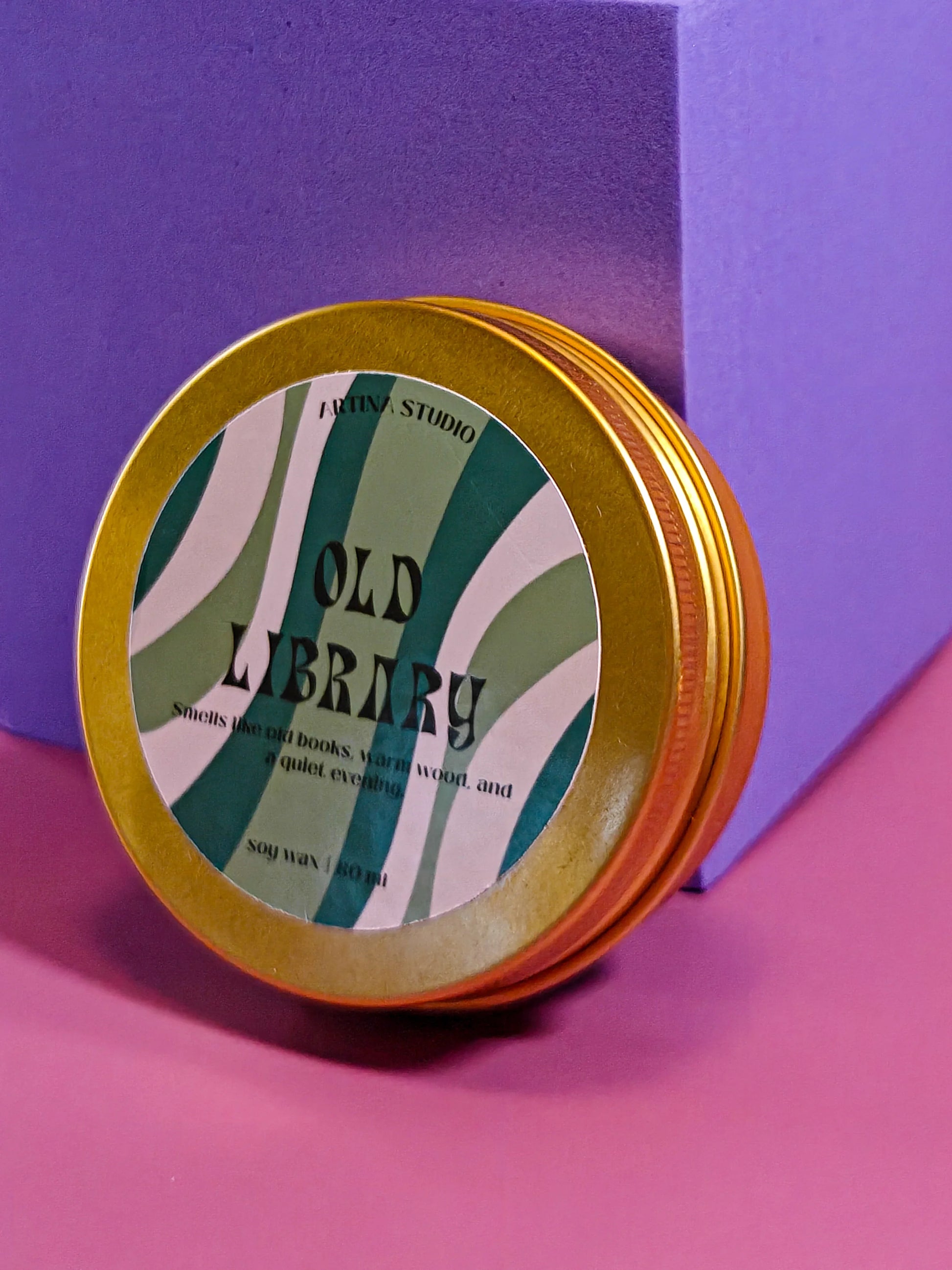 Gouden geurkaars in blik met label 'Old Library', op roze en paarse achtergrond.