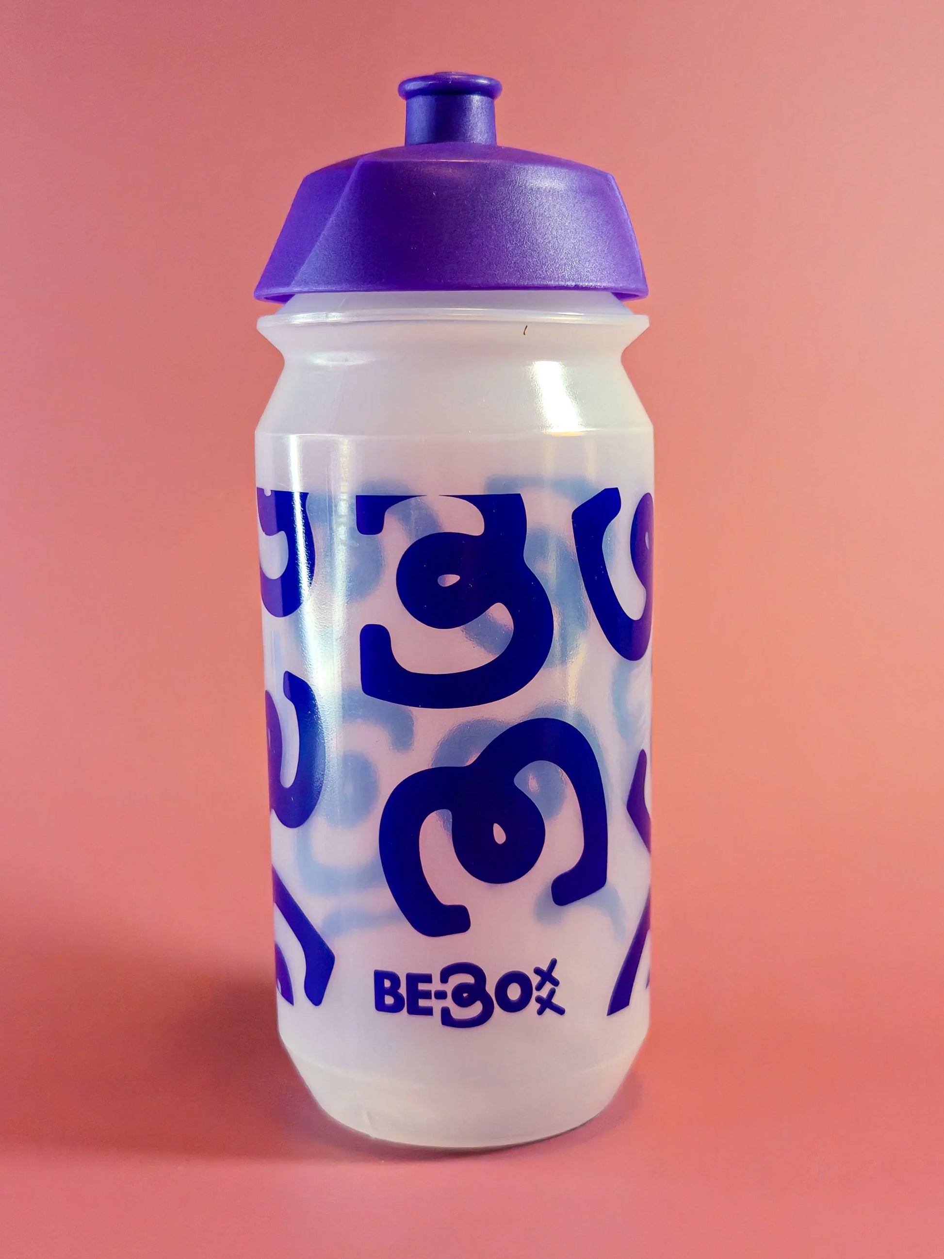 Transparante plastic sportbidon met paarse dop en blauwe grafische print, tegen roze achtergrond.