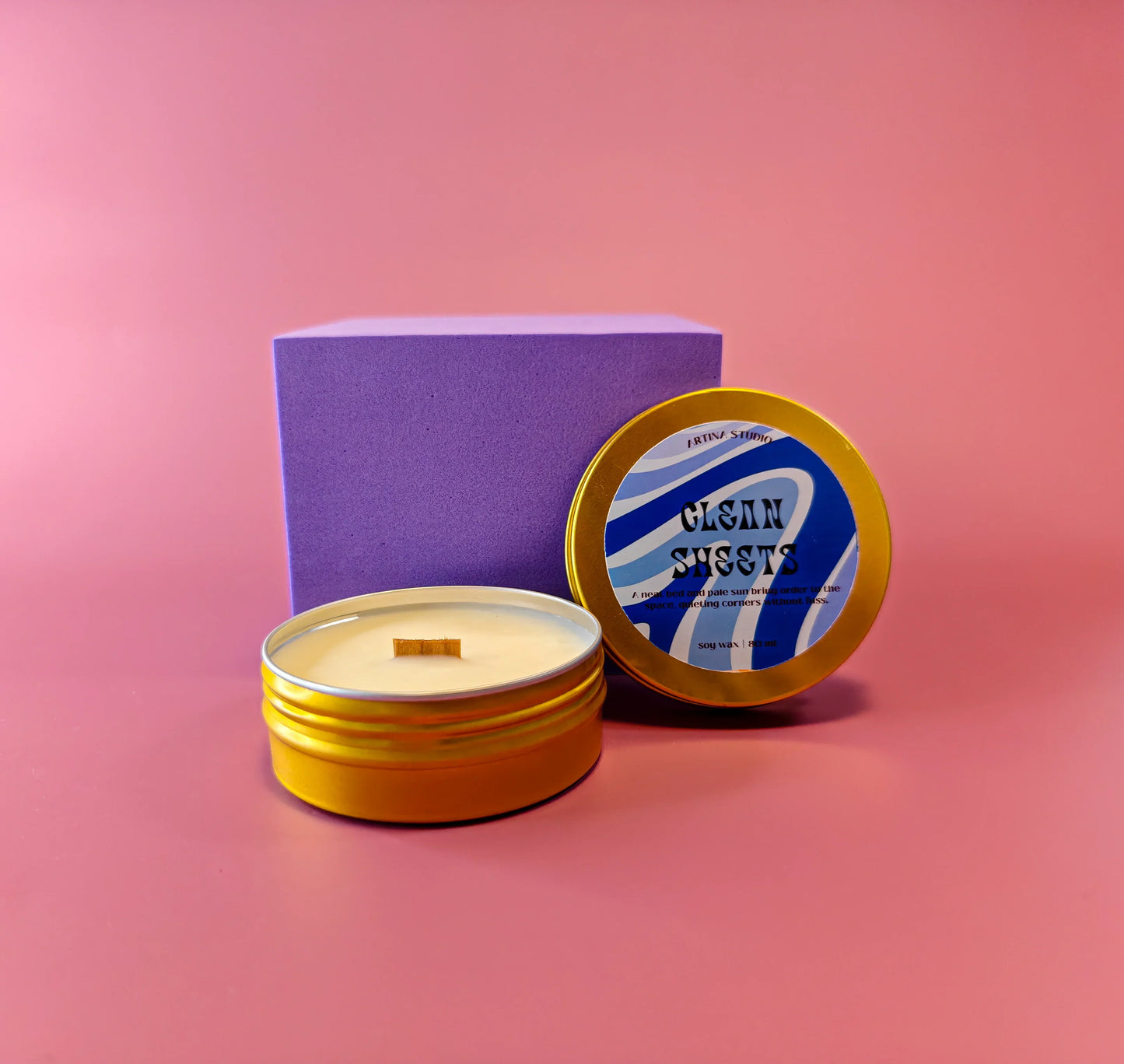 Sfeervolle soja geurkaars in goudkleurig blik met paarse giftbox op roze achtergrond