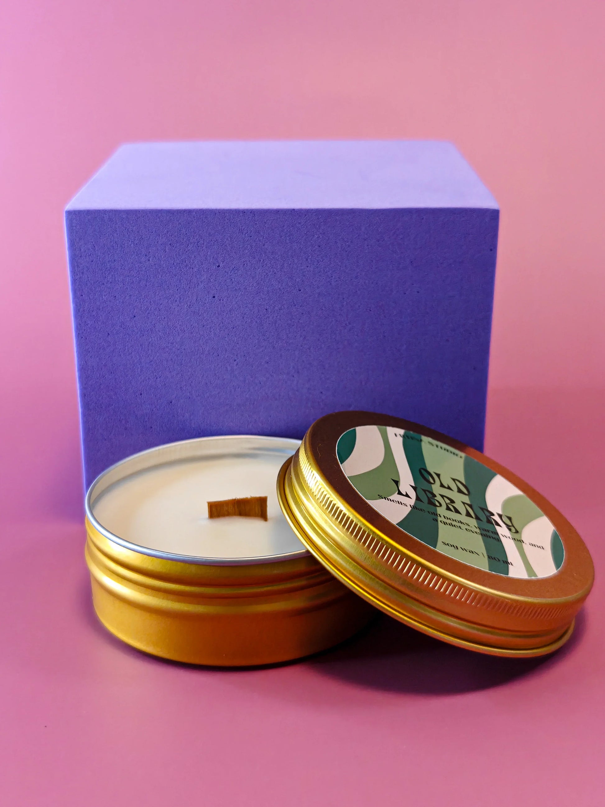 Gouden geurkaars in blik met houten lont voor cadeaubox, paarse doos, roze achtergrond