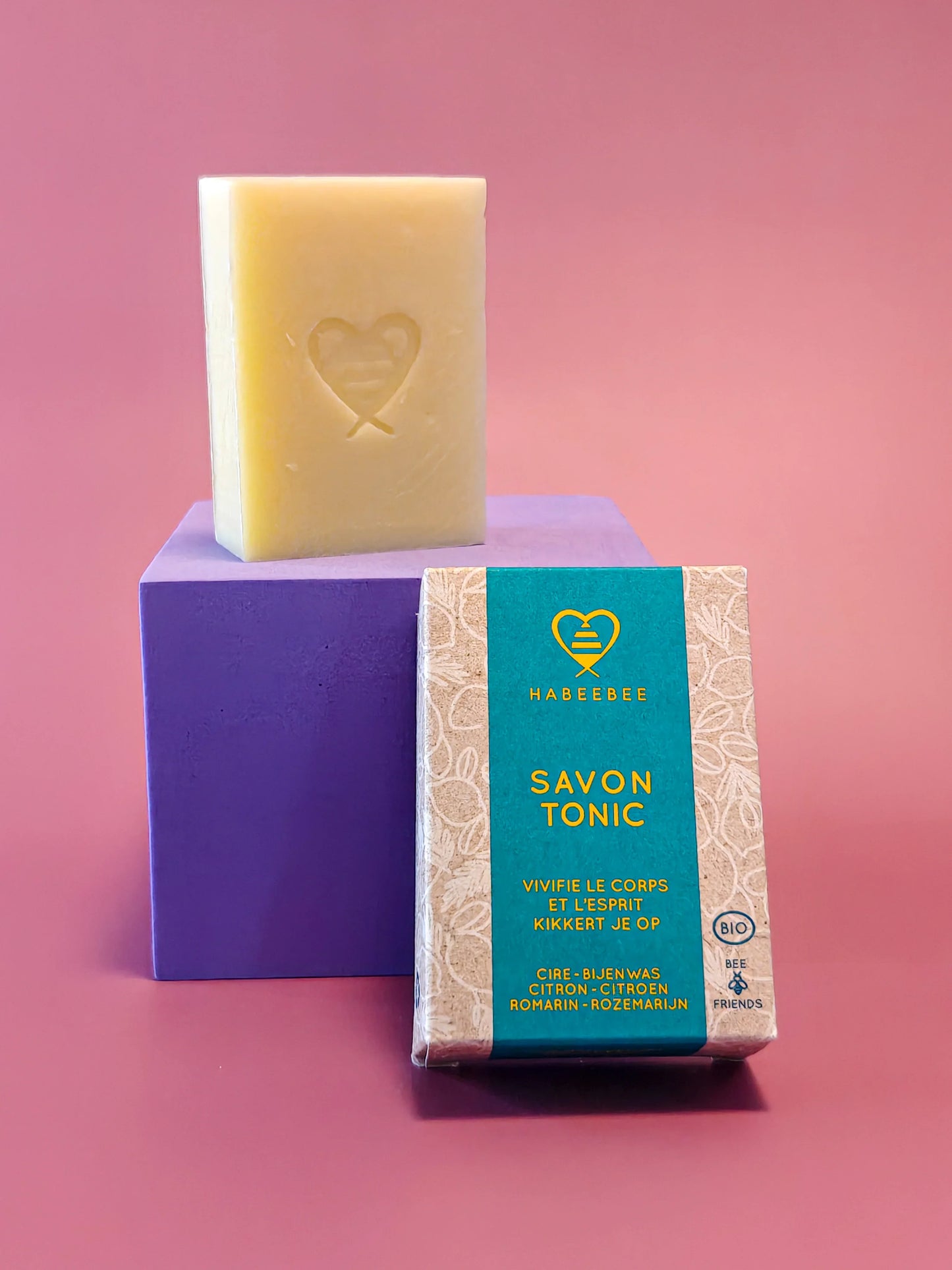 Handgemaakte Savon Tonic zeep met bijenwas, citroen en rozemarijn op roze en paarse achtergrond.