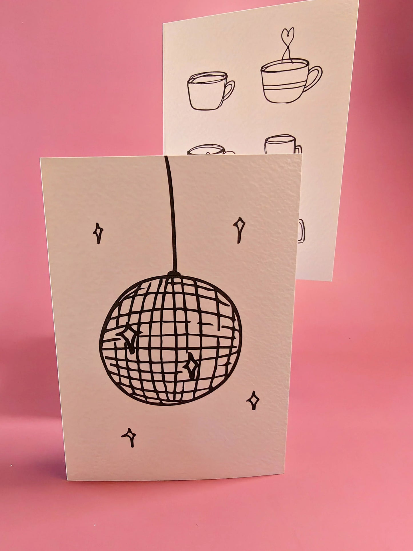 Twee minimalistische wenskaarten met disco bal en koffiekoppen illustraties, op roze achtergrond.