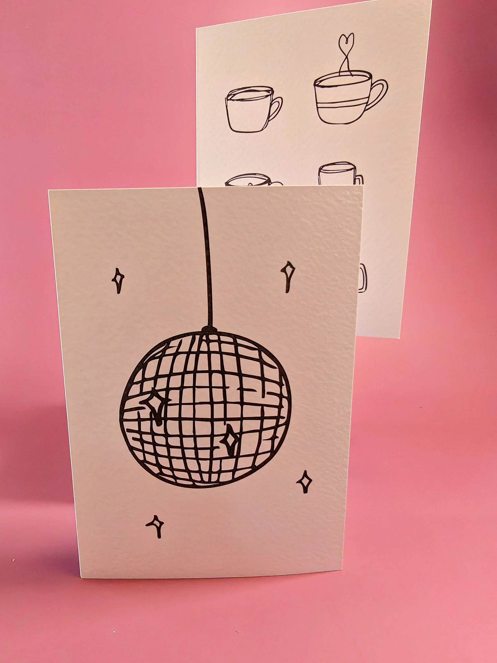 Twee minimalistische wenskaarten met disco bal en koffiekoppen illustraties, op roze achtergrond.