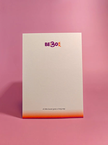 Minimalistische kaart met BE-Boxx logo op roze achtergrond, tekst 'A little boost goes a long way'.