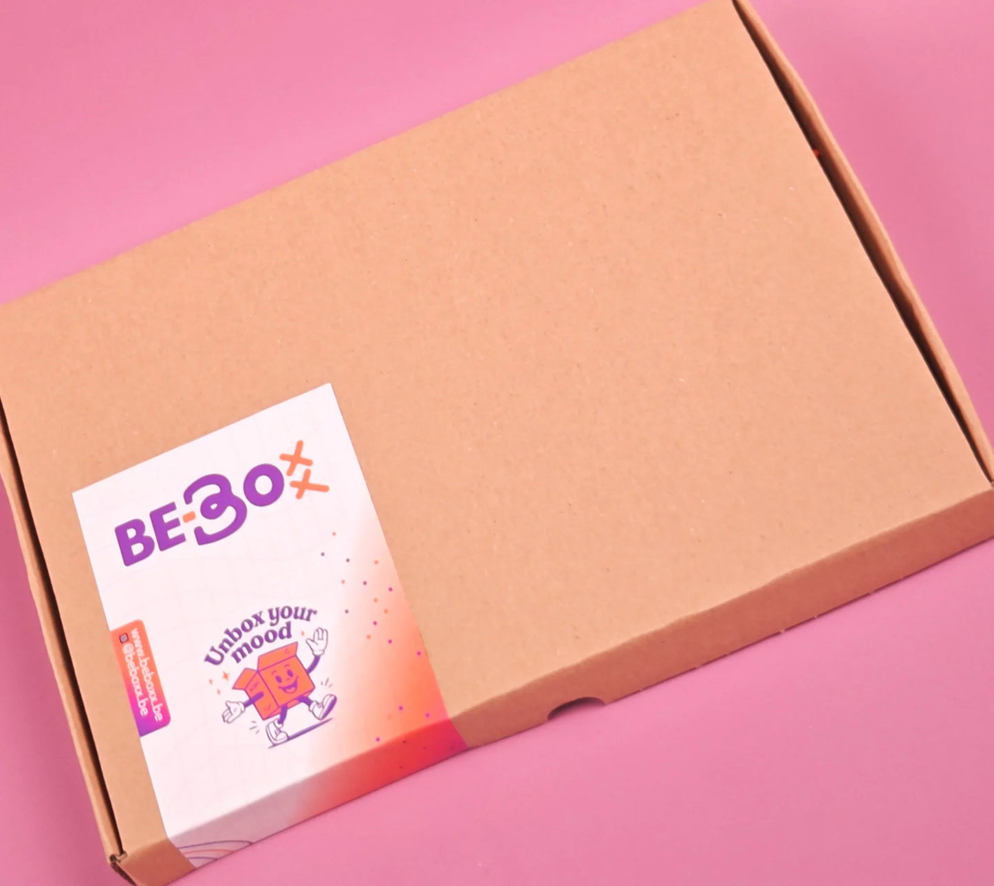 Cadeaubox van bruin karton met kleurrijke sticker op een roze achtergrond