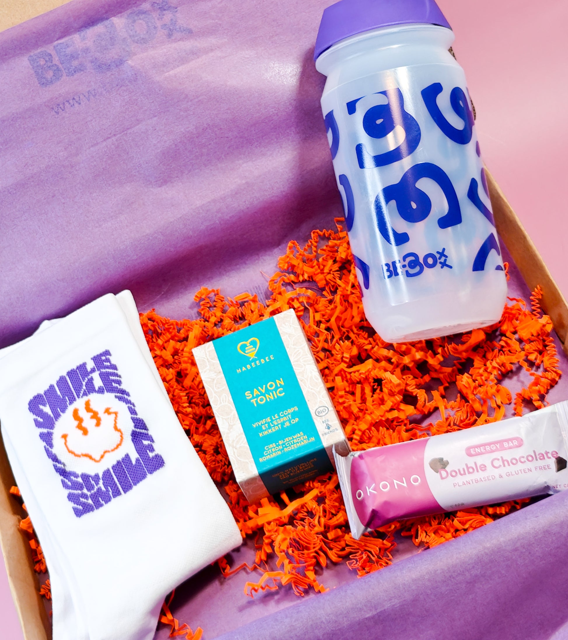 Cadeaubox met paarse shakerfles, witte sokken met opdruk, natuurlijke zeep en chocolade-energiebar.