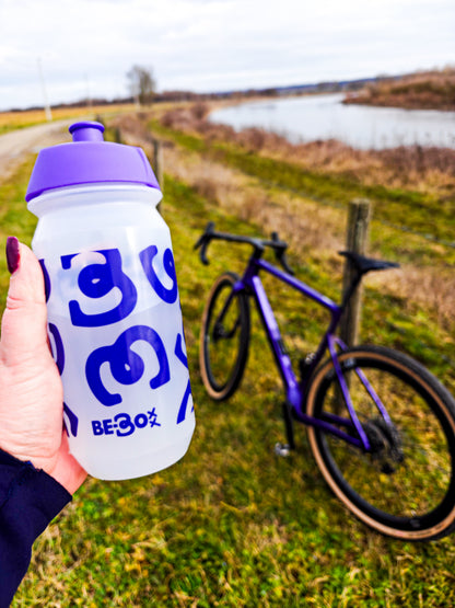 Transparante sportbidon met paars deksel en design, hand vast, racefiets buiten in natuur