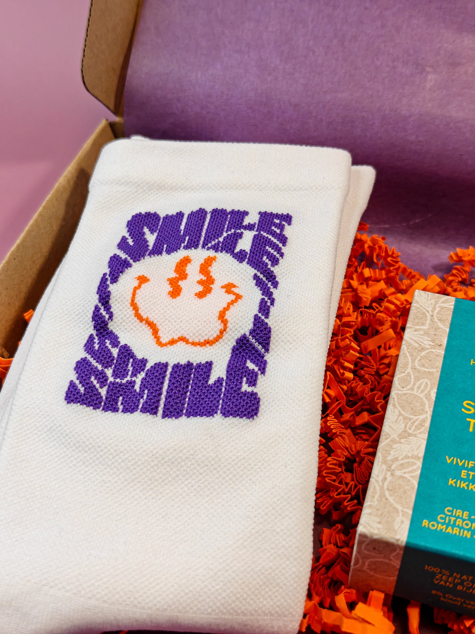 Witte sok met paarse SMILE tekst en oranje smiley in cadeaupakket met decoratief papier.