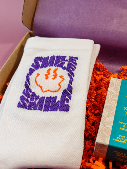 Witte sok met paarse SMILE tekst en oranje smiley in cadeaupakket met decoratief papier.